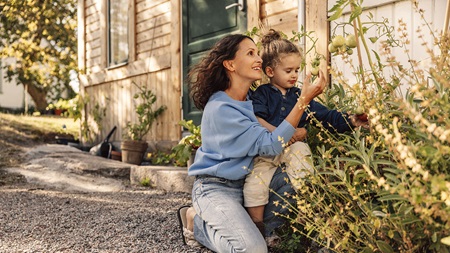 Kvinna och barn tittar på tomatodling vid husknuten.